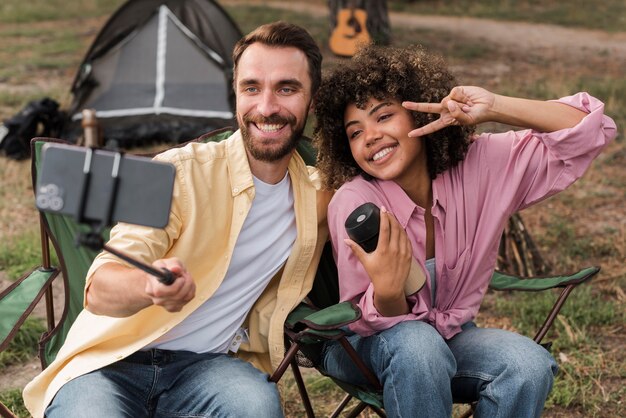 Pareja sonriente tomando selfie mientras acampa al aire libre