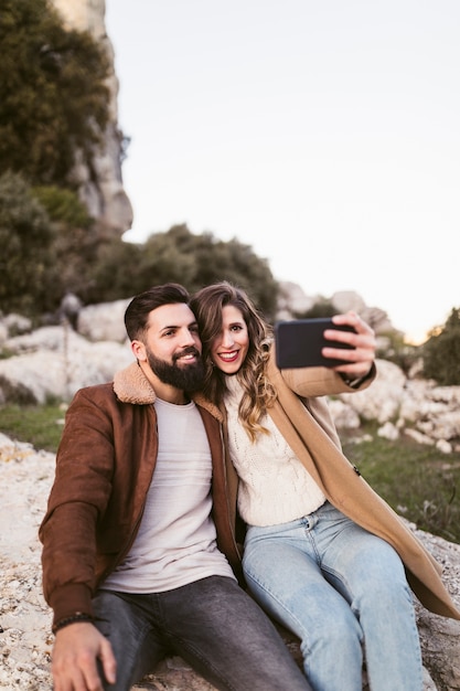 Pareja sonriente tomando un selfie en una roca