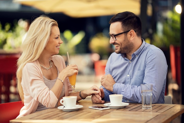 Pareja sonriente tomándose de la mano y hablando entre ellos mientras tienen una cita en un café