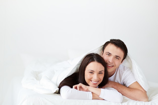 Pareja sonriente tumbada en la cama