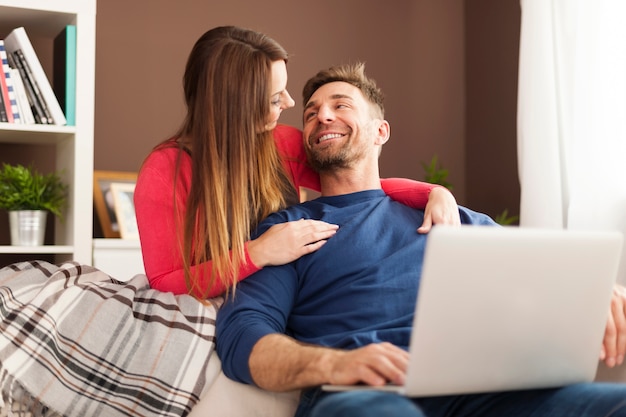 Pareja sonriente usando laptop en casa