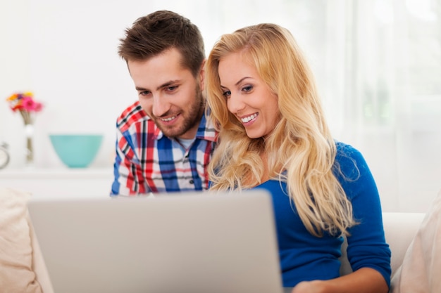 Pareja sonriente usando laptop en casa