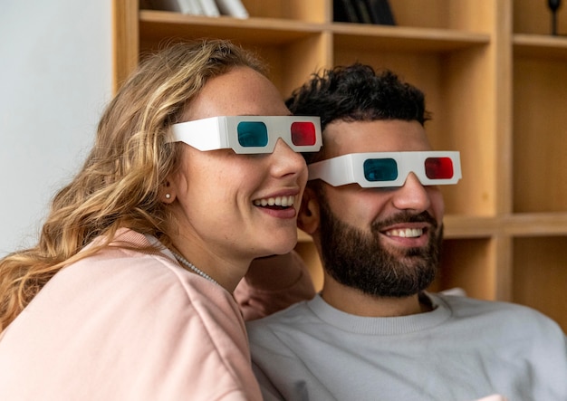 Pareja sonriente viendo películas en casa con gafas tridimensionales