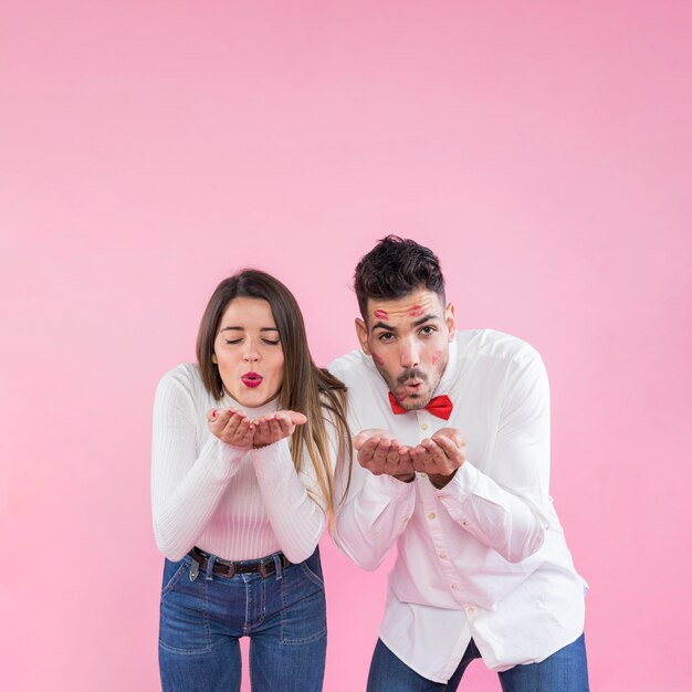 Pareja soplando besos sobre fondo rosa