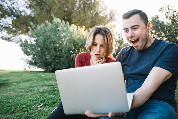 Pareja sorprendida usando la computadora portátil en el suelo