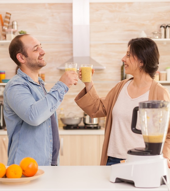 Pareja sosteniendo batido nutritivo en la cocina de sabrosas frutas. Estilo de vida saludable, despreocupado y alegre, comiendo dieta y preparando el desayuno en una acogedora mañana soleada