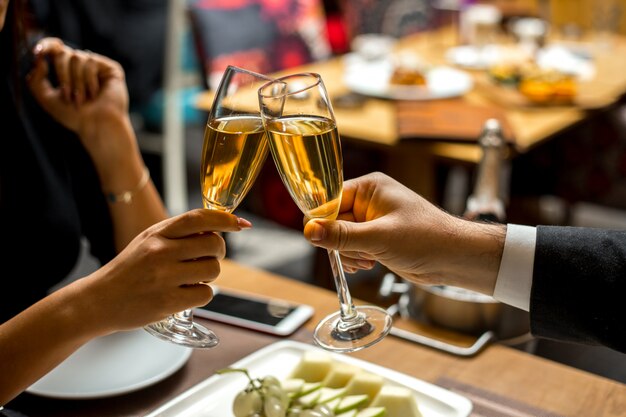 Pareja sostiene las copas con champán con vista lateral de plato de fruta