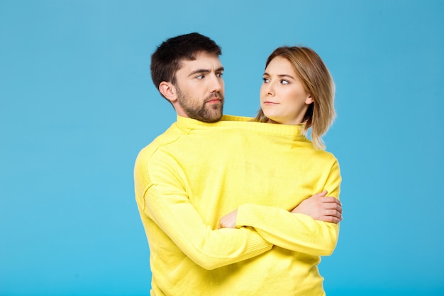 Pareja en suéter amarillo posando con los brazos cruzados sobre la pared azul