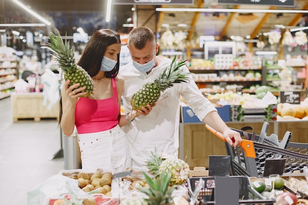 Pareja en un supermercado. Señora con una máscara médica. La gente hace parchases.