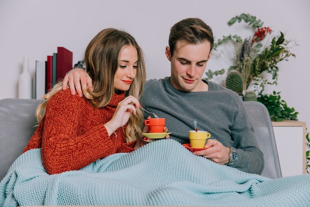 Pareja con tazas sentado en el sofá