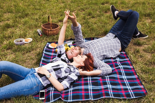 Pareja tendida en una manta sobre la hierba verde tomados de la mano de un picnic