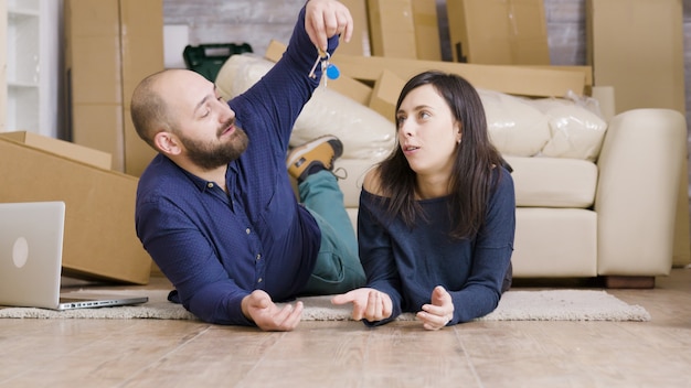 Pareja tendida en el suelo de su nuevo apartamento. Novio dando llaves a su novia.