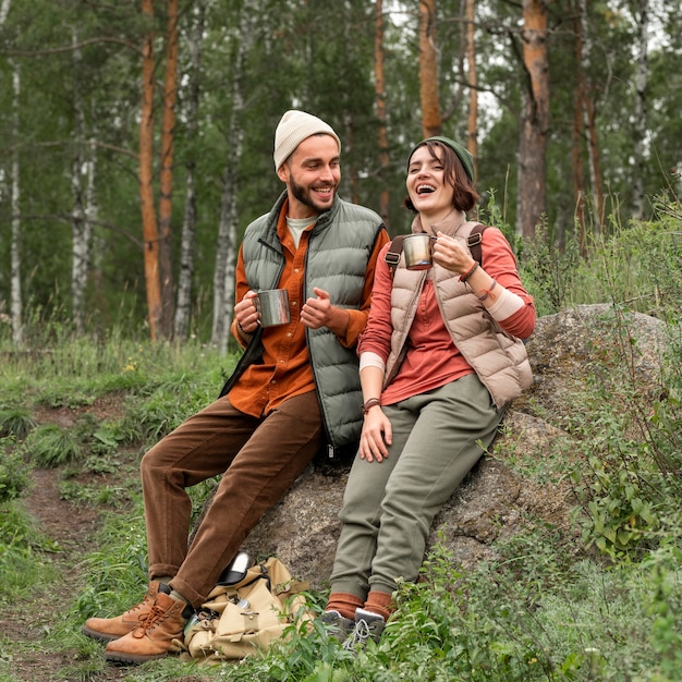 Pareja de tiro completo disfrutando de una bebida caliente en la naturaleza