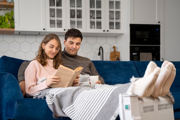 Pareja de tiro completo leyendo cerca del calentador