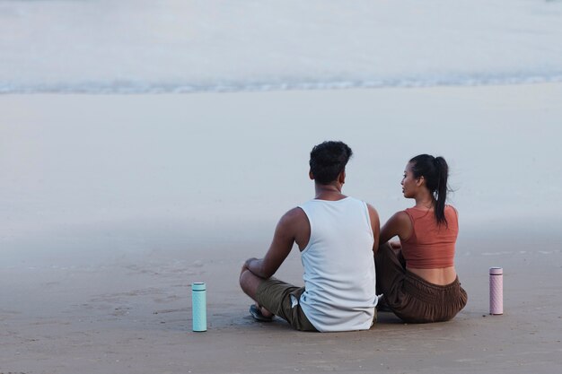 Pareja de tiro completo meditando en la playa