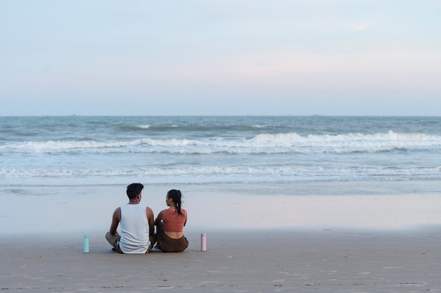 Pareja de tiro completo meditando en la playa