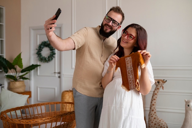 Pareja de tiro medio anunciando embarazo con teléfono inteligente