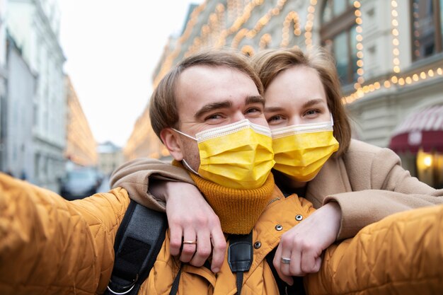 Pareja de tiro medio con máscaras tomando selfie