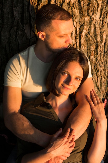 Pareja de tiro medio posando cerca de árbol