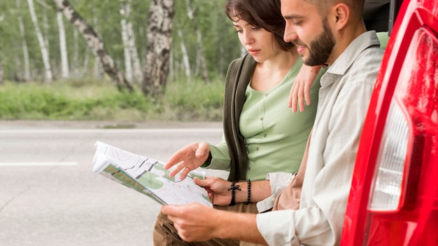 Pareja de tiro medio sentado en el maletero mirando en el mapa