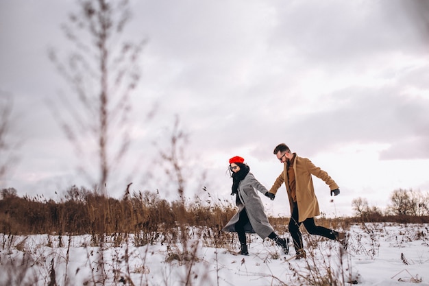 Pareja tomados de la mano corriendo por un parque de invierno