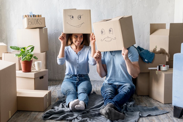 Foto gratuita pareja tonta con cajas sobre cabezas en casa el día de la mudanza