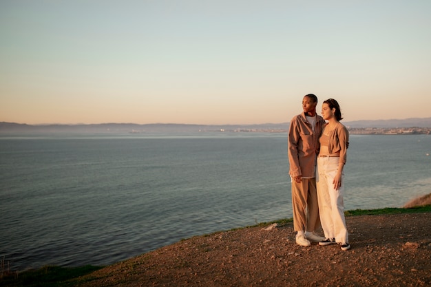 Foto gratuita una pareja trans abrazándose en la playa mientras contemplan la puesta de sol