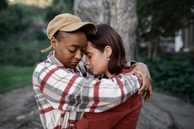 Foto gratuita pareja trans abrazándose y siendo afectuosa por un gran árbol en el parque