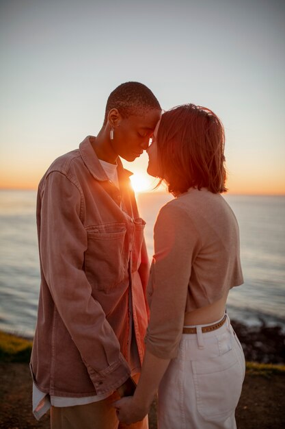 Pareja trans tomados de la mano al atardecer en la playa