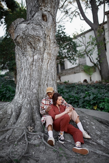 Foto gratuita pareja trans tomados de la mano mientras está sentado junto a un gran árbol en el parque