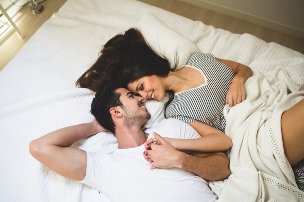 Pareja tumbada en la cama agarrada de la mano y mirándose a los ojos