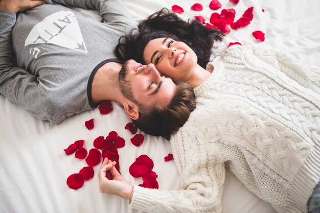 Pareja tumbada en la cama cabeza con cabeza rodeada de pétalos de rosa