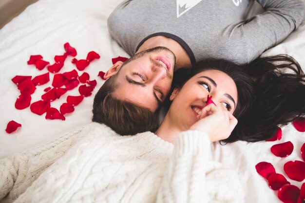 Pareja tumbada en la cama cabeza con cabeza rodeada de pétalos de rosa