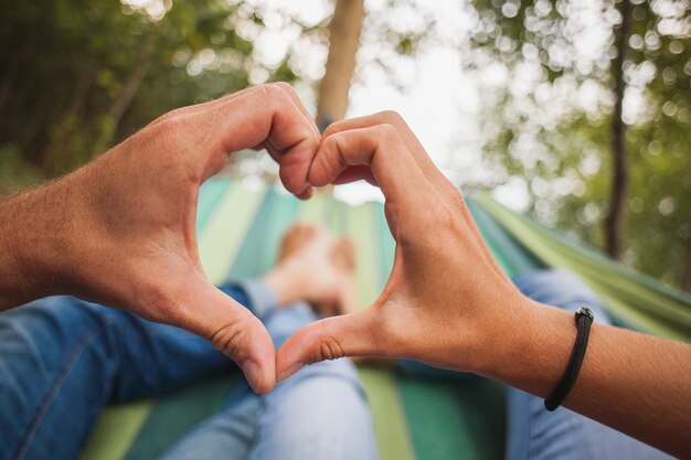 Pareja tumbada en una hamaca haciendo el símbolo del corazón