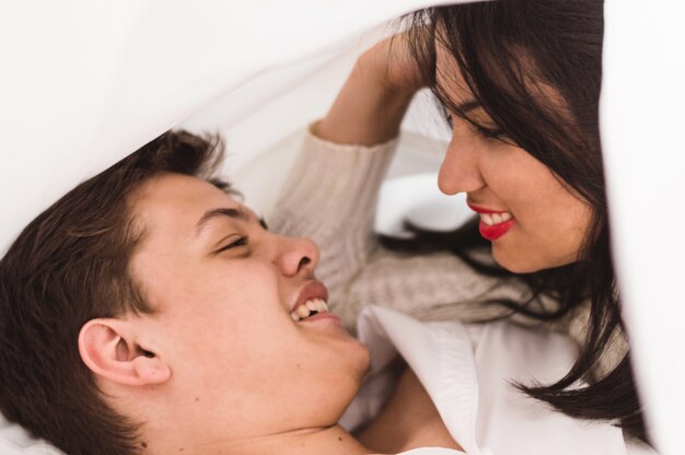 Pareja tumbada mirándose a los ojos mientras sonríen