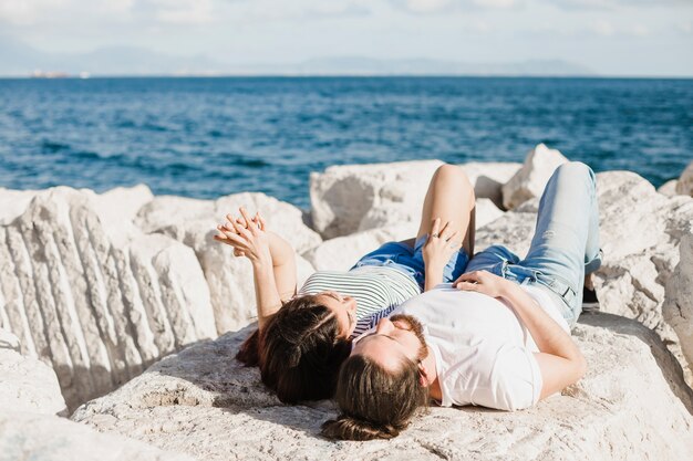 Pareja tumbada en rocas por el mar