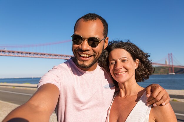 Pareja de turistas alegres tomando selfie en el paseo de la ciudad