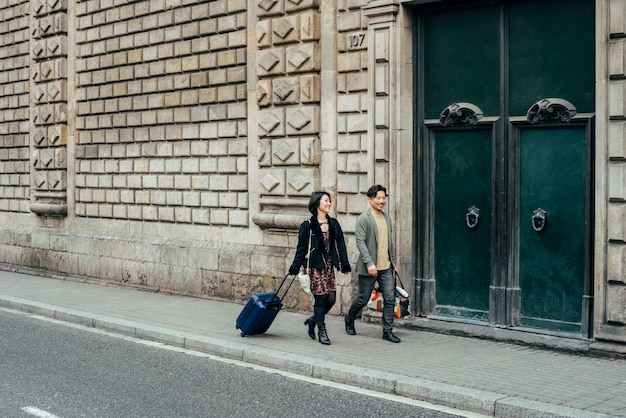 Pareja de turistas felices asiáticos caminando con maleta