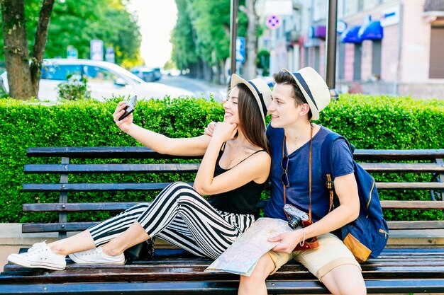 Pareja de turistas jóvenes en banco haciendo un selfie