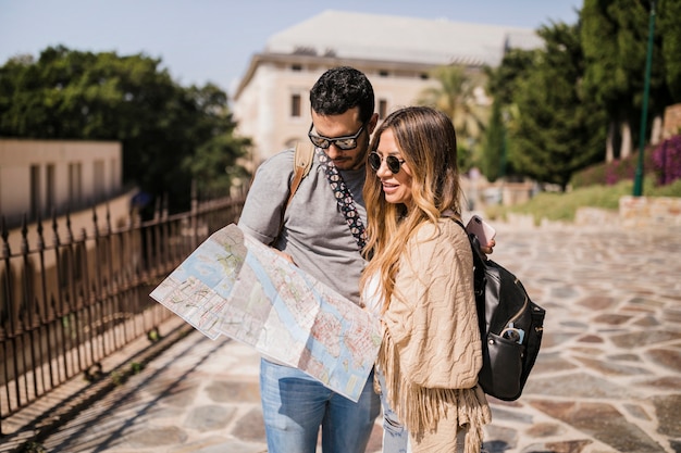 Pareja de turistas jóvenes de pie en la calle mirando el mapa