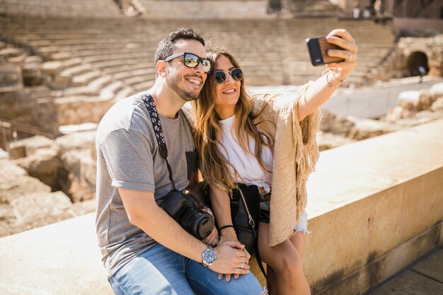 Pareja de turistas sentados juntos tomando selfie a través del teléfono celular