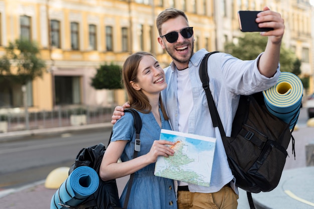 Pareja de turistas sonrientes tomando selfie mientras llevaba mochilas
