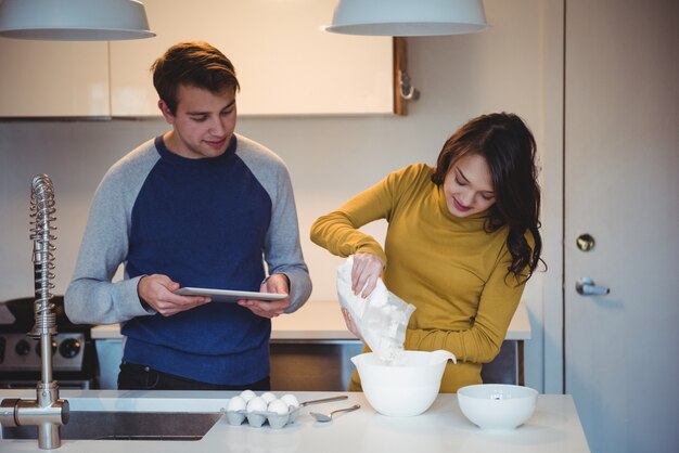 Pareja usando tableta digital mientras prepara galletas en la cocina