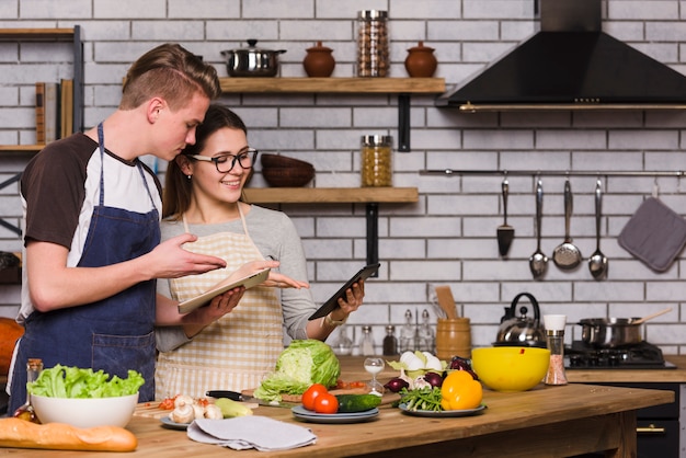 Pareja usando tabletas digitales mientras prepara comida