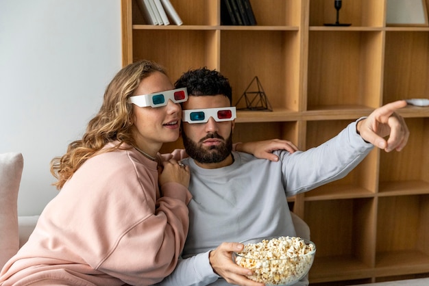 Pareja viendo películas en casa con gafas tridimensionales y comiendo palomitas de maíz