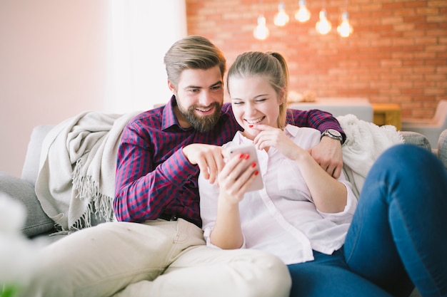 Pareja viendo el teléfono inteligente en el sofá