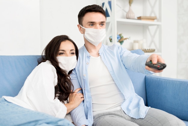 Pareja viendo televisión en casa con mascarillas