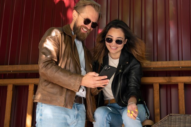 Foto gratuita pareja vistiendo chaquetas de cuero sintético y usando un teléfono inteligente al aire libre