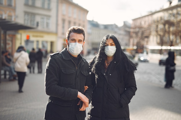 Foto gratuita pareja vistiendo una máscara protectora de pie en la calle