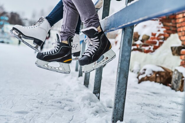 Pareja vistiendo patines de hielo sentados en una barandilla. Citas en una pista de hielo. Vista cercana de los patines